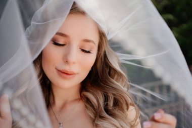 Duvağın altında uzun dalgalı saçları olan güzel bir gelin. Düğün makyajı.. 