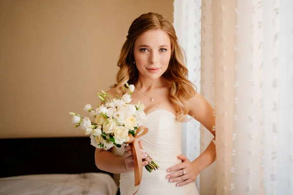 Porträt einer schönen Braut mit einem Strauß am Fenster. Hochzeitstraditionen. — Stockfoto
