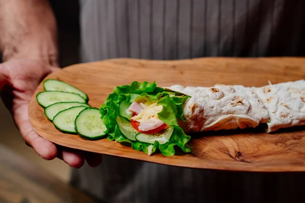Pita with vegetables and chopped cucumbers on a cutting board in the hands — Stock Photo, Image
