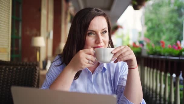 Mulher feliz senta-se com laptop no café na rua e bebe café — Vídeo de Stock
