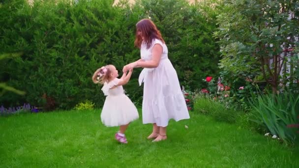 Mutter und Tochter in weißen Kleidern haben Spaß und spielen auf dem Rasen im Hinterhof — Stockvideo
