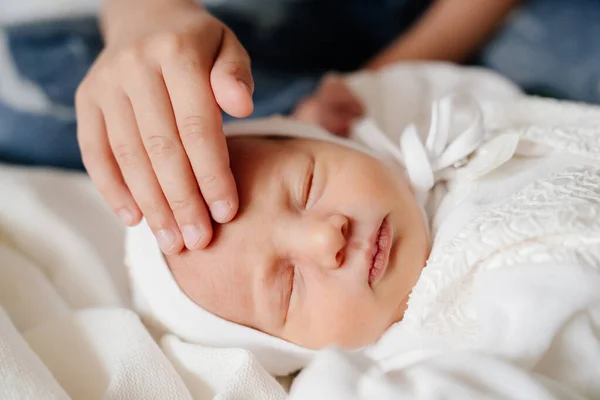 Dětská ruka hladí hlavu Novorozené dítě v bílém oblečení. — Stock fotografie
