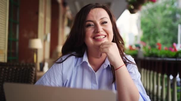 Mulher feliz senta-se com laptop no café na rua, se comunica com o amigo — Vídeo de Stock