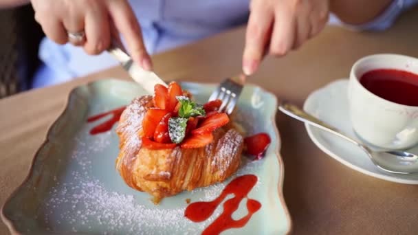 Kezek közelről. Egy nő eperrel, mentával és lekvárral eszik croissant-t. — Stock videók