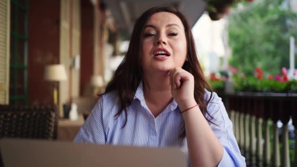 Mulher feliz senta-se com laptop no café na rua, se comunica com o amigo — Vídeo de Stock
