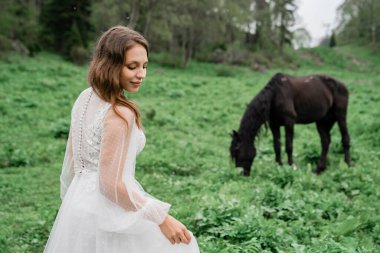 Beyaz gelinlikli güzel bir kadın atlarla birlikte bir tarlada duruyor..