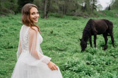 Beyaz gelinlikli güzel bir kadın atlarla birlikte bir tarlada duruyor..