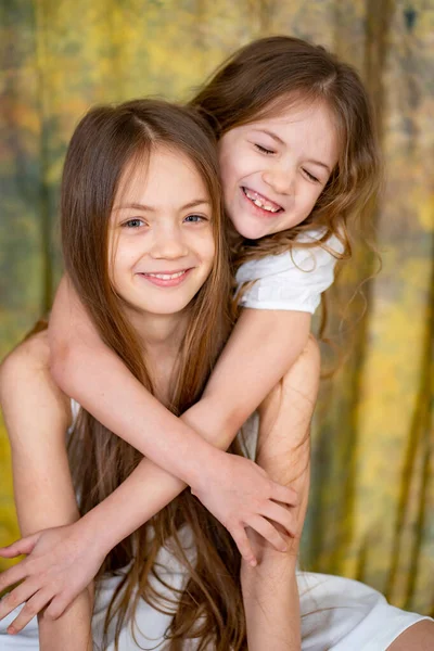Duas meninas com cabelos longos em roupas brancas se abraçam. amor entre irmãs. — Fotografia de Stock