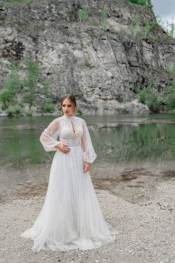 Dağ nehrinin kıyısında beyaz gelinlikli gelin..