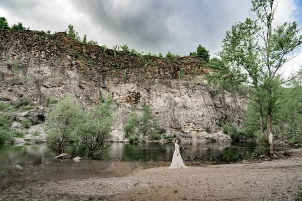 A noiva em um vestido de casamento branco na margem de um rio de montanha. — Fotografia de Stock