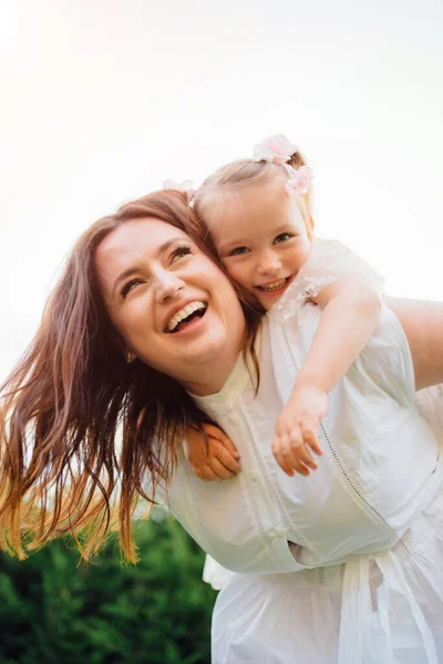 Mamá y su hija en vestidos blancos divertirse, jugar y abrazar en el césped — Foto de Stock