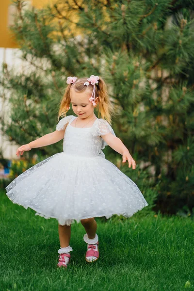 Šťastná holčička v bílých šatech spinning a tanec na trávníku v zahradě — Stock fotografie