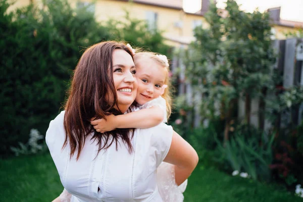 Mamá y su hija en vestidos blancos divertirse, jugar y abrazar en el césped — Foto de Stock