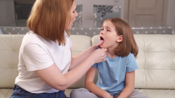 La niña se queja de un dolor de garganta y su madre lo examina. — Vídeo de stock