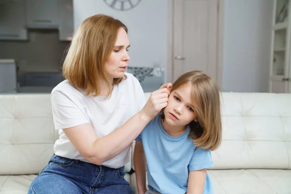 Una niña se queja de dolor de oído y su madre lo examina. enfermedades infantiles. — Foto de Stock