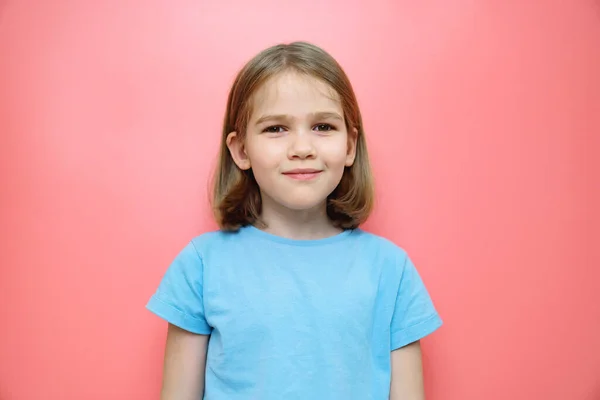 Porträtt av en liten flicka i en blå T-shirt på en rosa bakgrund. — Stockfoto