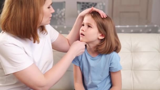 La niña se queja de un dolor de garganta y su madre lo examina. — Vídeos de Stock