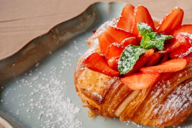 Çilekli kruvasan, beyaz tabakta nane ve pudra şekeri..