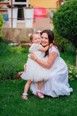 Beyaz elbiseli anne ve kız çimlerin üzerinde oynaşıp oynaşıyorlar.