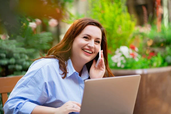 Kobieta siedzi na zewnątrz kawiarni i pracuje na laptopie i rozmawia przez telefon — Zdjęcie stockowe