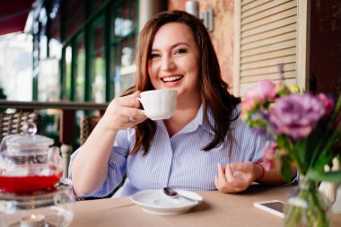 Güzel bir kadın kafedeki verandada çay içiyor.