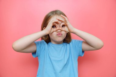 Eller gözlük ya da dürbün gibi katlıdır. Pembe arka planda mavili kız. 