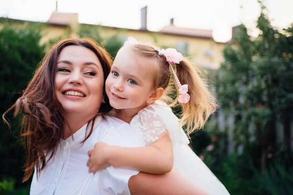 Mamá y su hija en vestidos blancos divertirse, jugar y abrazar en el césped — Foto de Stock