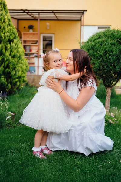 Mamá y su hija en vestidos blancos divertirse, jugar y abrazar en el césped — Foto de Stock