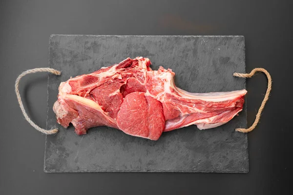 Trozo de carne de res en el hueso en la tabla de cortar piedra negro. productos agrícolas —  Fotos de Stock