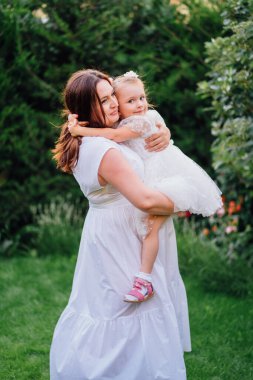Beyaz elbiseli anne ve kız çimlerin üzerinde oynaşıp oynaşıyorlar.