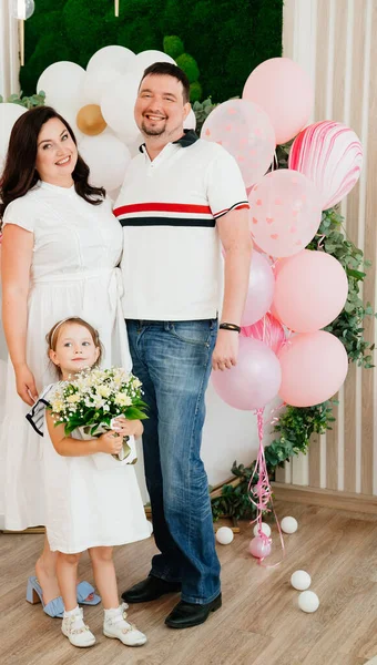 Pappa och mamma med dotter i vit klänning står på fotozon med ballonger — Stockfoto