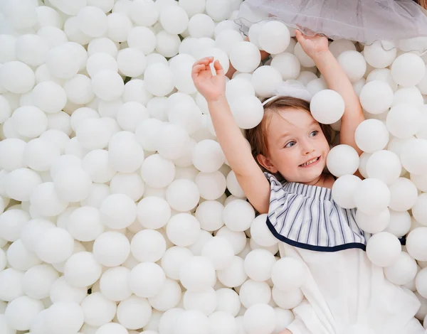 Niña alegre en una piscina seca con bolas blancas. parque infantil. — Foto de Stock
