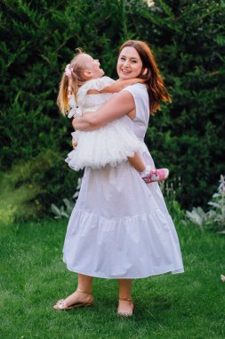 Beyaz elbiseli anne ve kız çimlerin üzerinde oynaşıp oynaşıyorlar.