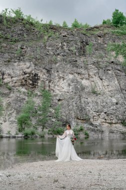 Dağ nehrinin kıyısında beyaz gelinlikli gelin..
