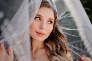 Duvağın altında uzun dalgalı saçları olan güzel bir gelin. Düğün makyajı.. 