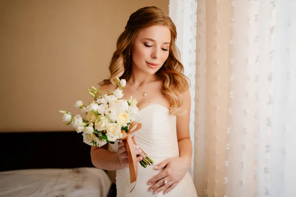 Porträt einer schönen Braut mit einem Strauß am Fenster. Hochzeitstraditionen. — Stockfoto