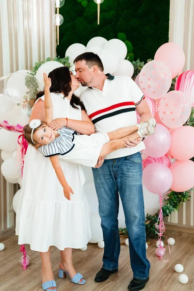 Pappa och mamma med dotter i vit klänning står på fotozon med ballonger — Stockfoto