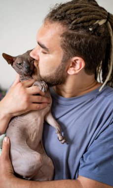 Rastalı ve sakallı bir adam safkan kel bir kediyi öper.. 