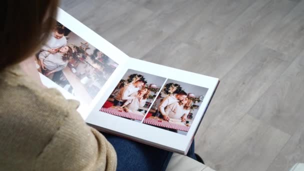 Woman flips through the pages of photobook from a new years family photo shoot — Stock Video