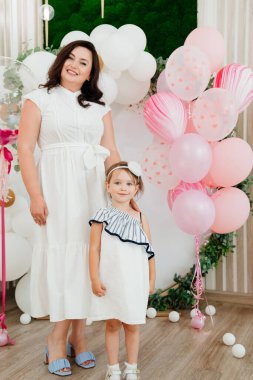 Beyaz elbiseli anne balonlarla fotoğraf bölgesinde duruyor.