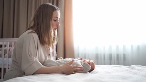 Mãe mudando de vestido bebê na cama no quarto. bens e roupas para recém-nascidos. — Vídeo de Stock