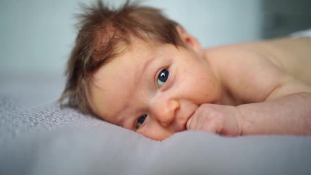 Een pasgeboren baby ligt op het bed en houdt zijn hand in zijn mond. — Stockvideo