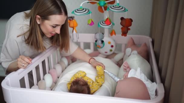 Moeder staat bij de wieg van een pasgeboren baby. meubels en speelgoed voor kinderen kamer. — Stockvideo