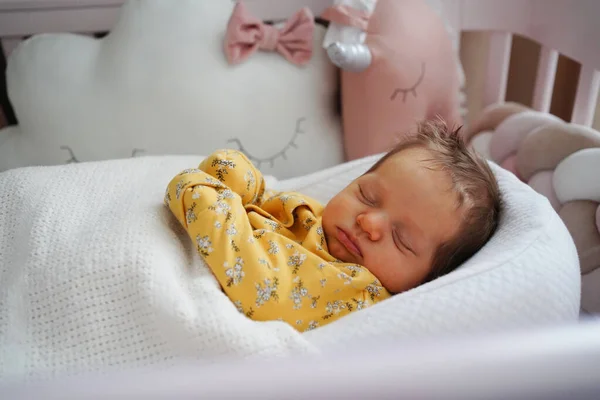 Recién nacido en un mono amarillo se encuentra en un retenedor del niño en una cuna — Foto de Stock