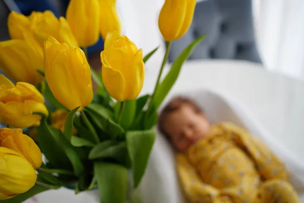 Έμφαση στα άνθη. Το νεογέννητο μωρό με κίτρινη φόρμα βρίσκεται σε ένα στήριγμα για το παιδί — Φωτογραφία Αρχείου