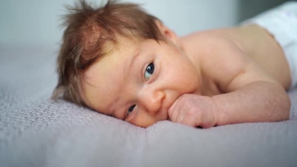 Un bebé recién nacido se acuesta en la cama y sostiene su mano en su boca. — Vídeo de stock