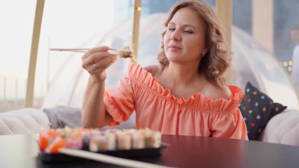 Eine attraktive Frau isst Brötchen mit Stöcken. Lieferung von Lebensmitteln aus dem Restaurant — Stockvideo