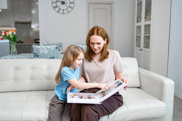 Madre e hija mirando un libro con fotos de una sesión de fotos de la familia — Foto de Stock