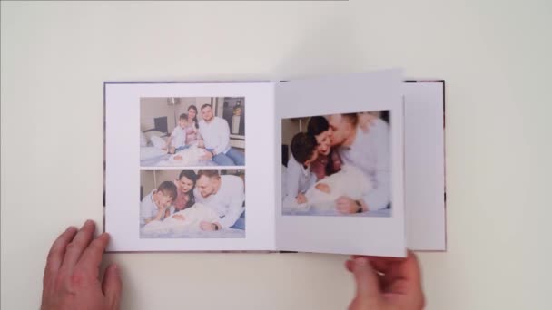 Auf weißem Hintergrund, Hände blättern durch Fotobuch vom Familienfotoshooting — Stockvideo