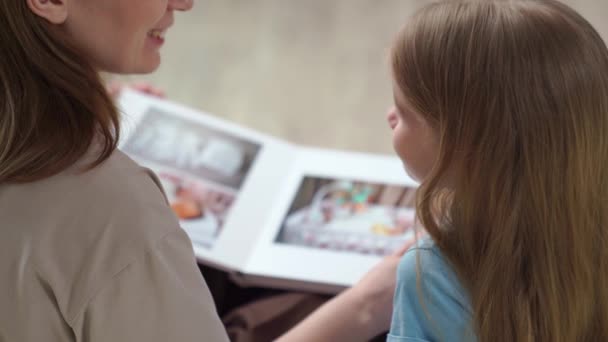 Vue de dessus. mère et fille regardant livre avec des photos de la séance photo de famille — Video